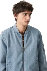 Campera tipo bomber confeccionada en denim lavado, con cierre frontal, cuello, puños y ruedo en tejido rib elástico. Presenta bolsillos laterales y un bolsillo utilitario con cierre en la manga izquierda.