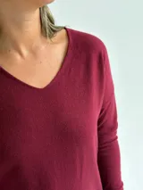 Sweater de punto en color bordó, con escote en V, mangas largas y diseño de corte recto con dobladillo ligeramente más largo en la parte posterior.