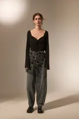 Falda mini de tiro alto confeccionada en denim gris oscuro con efecto lavado. Presenta un diseño superpuesto de tul negro con bordados florales y lentejuelas, además de detalles de tachas metálicas a lo largo de las costuras laterales.