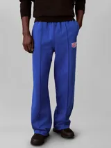 Pantalón de felpa azul con cintura elástica, pierna recta y costuras delanteras decorativas. Cuenta con un pequeño bordado en el muslo.
