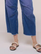 Jean wide leg cropped de tiro medio-alto, confeccionado en denim azul intermedio con efecto degradé y costuras en tono camel. Presenta cinco bolsillos, cierre frontal con botón y cierre, nervaduras decorativas en la zona de las rodillas y ruedo desflecado.
