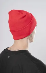 Gorro de tejido tipo beanie, color rojo, con borde doblado y un pequeño parche negro bordado con un símbolo de tijeras cruzadas en blanco.