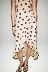 Vestido midi de mezcla de lino y viscosa en color beige con estampado de lunares bordó. Cuenta con escote recto, tirantes anchos y un volante lateral en cascada que recorre el frente hasta el bajo asimétrico.
