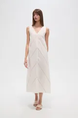 Vestido midi de algodón color crudo, con cuello en V, sin mangas y diseño holgado. Presenta un delicado bordado lineal en forma de zigzag que recorre toda la prenda.