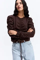 Blusa de manga larga color marrón chocolate, con diseño fruncido central ajustable mediante cordones y mangas con detalle de frunces laterales que aportan volumen.