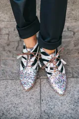 Botines acordonados con estampado de cebra en blanco y negro, puntera cubierta de glitter multicolor y suela plana color madera.