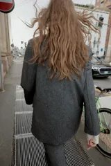 Blazer recta gris con hombreras, cuello solapa, manga larga, bolsillos delanteros con solapa y cierre frontal con un botón.