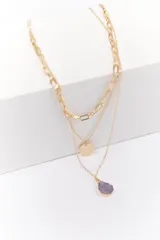 Collar dorado de tres cadenas con dijes: una cadena de eslabones grandes, una cadena fina con un dije redondo con diseño de rayos de sol y una cadena fina con un dije de piedra irregular color lila.