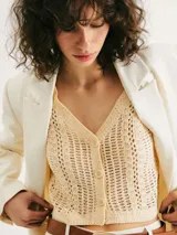 Chaleco de punto calado en color beige, con escote en V y cierre frontal con botones. Presenta un diseño sin mangas y corte recto.