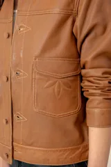 Campera de cuero marrón, con cuello camisero, cierre frontal con botones metálicos y bolsillos frontales.