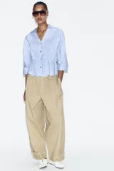 Pantalón de tiro alto en color beige, con pinzas delanteras, bolsillos laterales y bajo con vuelta. Presenta un cierre frontal con cremallera, botón interior y gancho.