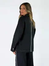Blazer de lino color marrón con solapa clásica, cierre frontal de tres botones, bolsillos aplicados con solapa y costuras pespunteadas en contraste.