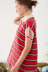 Vestido tipo polo corto tejido de punto, con diseño de rayas horizontales en tonos rojo, marrón y blanco, cuello y escote V en color tostado, y mangas cortas holgadas.