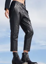 Pantalón sastrero de ecocuero negro, con corte recto, bolsillos delanteros y traseros, y botamanga irregular más corta en la parte frontal.