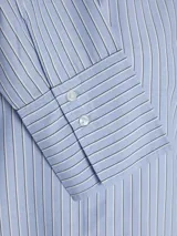 Camisa de manga larga con cuello clásico y cierre frontal de botones. Presenta un diseño a rayas verticales en tonos celestes y blancos, con puños anchos y un corte relajado.