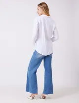 Camisa blanca de rayón con cuello solapa, escote en V y cierre frontal con botones. Presenta plisados verticales en la parte delantera y un canesú con tablón central en la espalda. El bajo es redondeado y ligeramente más largo en la espalda.