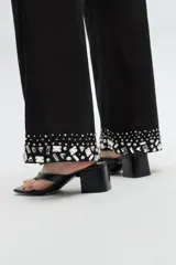Pantalón de corte recto y tiro medio, color blanco, con detalle de pedrería brillante en el ruedo y costuras verticales decorativas.