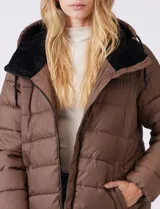 Campera puffer color marrón con capitoneado horizontal. Tiene cuello alto y capucha ajustable con cordones, con el interior del cuello en textura aterciopelada negra. Cierre frontal completo y bolsillos laterales. El corte es ligeramente más largo en la parte posterior con aberturas laterales redondeadas.