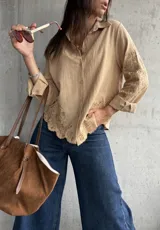 Camisa de lino color camel con cuello clásico, cierre frontal de botones y mangas largas. Presenta un delicado bordado floral tono sobre tono en las mangas y en el ruedo, el cual tiene un acabado festoneado.