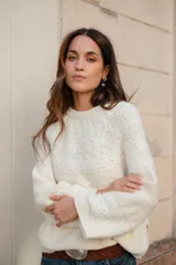 Buzo tejido de punto con cuello redondo, manga larga y diseño holgado. Presenta tajos laterales y un corte asimétrico, siendo ligeramente más largo en la parte posterior.