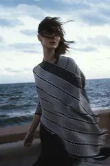 Ruana tejida con rayas horizontales en tonos de gris y negro, con cuello alto y mangas cortas.