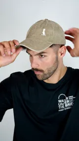Gorra tipo baseball color beige con efecto desgastado, presenta un pequeño bordado blanco en el panel frontal.