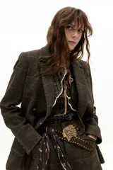 Chaqueta de doble botonadura con diseño de cuadros en tonos verde oscuro y líneas rojizas. Presenta solapas clásicas, bolsillos frontales tipo plaqué, tajo en la espalda y botones de cuero.