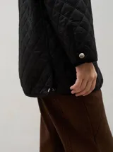 Campera acolchada de corte holgado, color blanco con diseño capitoneado en forma de rombos. Presenta cuello camisero y bordes internos con estampado floral en tonos azul y rojo, cierre frontal con botones a presión y bolsillos laterales.