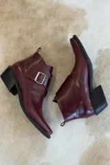Botin de cuero color bordeaux con diseño de textura combinada, punta cuadrada y hebilla metálica lateral.