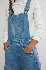 Jardinero enterito de denim en color azul claro, con diseño de peto, tiras regulables y botones laterales. Presenta corte amplio estilo barrel con piernas abuchonadas y bolsillos frontales.
