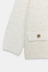 Chaqueta de punto en tono celeste, de cuello redondo, manga francesa y cierre frontal con botones dorados. Cuenta con bolsillos simulados con solapa y botones dorados en la parte delantera.