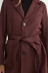 Chaqueta de gamuza sintética color bordó, con cuello solapa, cierre frontal de botones y cinturón ajustable del mismo material. Posee bolsillos frontales y mangas largas.