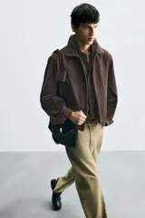 Cazadora cropped fit color marrón oscuro, confeccionada en tejido de algodón. Presenta cuello solapa, manga larga con puño abotonado, bolsillos de vivo en la cadera y un bolsillo interior. El bajo tiene elástico en la espalda y el cierre es frontal con cremallera.