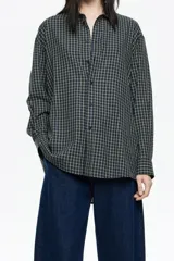 Camisa larga de corte recto, confeccionada en algodón, con patrón de cuadros pequeños en tonos azul marino y amarillo claro. Presenta cuello camisero, cierre frontal con botones y mangas largas con puño y botonadura.