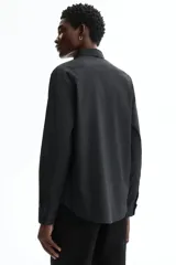 Camisa de vestir negra con cuello italiano, cierre frontal de botones y mangas largas con puños ajustables. Presenta un corte entallado y bajo redondeado.