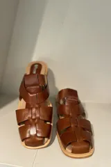 Zuecos negros de cuero charol con diseño de tiras entrecruzadas y suela plana.