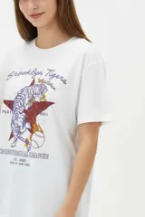 Remera de algodón negra de manga corta y cuello redondo, con estampa frontal que incluye letras rojas y gráficos en tonos dorados.