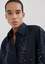 Camisa azul marino de lyocell y poliéster, con cuello camisero, manga larga, cierre frontal oculto con tapeta y detalles de apliques de strass y cristal en la parte delantera y las mangas.