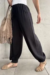Pantalón negro tipo babucha con cintura elástica fruncida y cordón ajustable, corte holgado y puños elásticos en los tobillos.