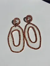 Aros colgantes plateados con diseño de doble óvalo concéntrico y detalle circular en el lóbulo, completamente recubiertos de cristales brillantes.
