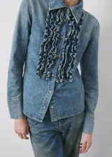 Camisa de denim estilo vaquero, con cuello camisero, manga larga con puños abotonados, cierre frontal con botones y detalle de volantes en el frente.