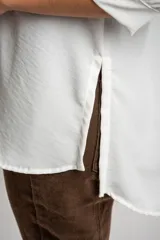 Blusa de corte oversize en color blanco, con cuello camisero, cierre frontal de botones y mangas tres cuartos con sutiles frunces en los hombros.