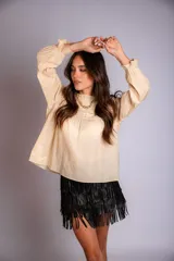 Camisa blanca de manga larga con detalles de encaje o bordado en el canesú y el frente. Presenta un corte holgado y mangas con puños elásticos o fruncidos.