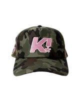 Gorra tipo trucker con frente rígido estampado en camuflado y parte trasera de malla. Presenta un bordado frontal con la letra K en color rosa con borde blanco.