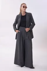 Pantalón de vestir de corte sastrero y pierna ancha (wide leg), confeccionado en tejido de lana gris. Presenta cintura alta con doble botón y pinzas frontales que aportan volumen y caída fluida.