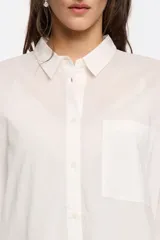 Camisa blanca de corte recto con cierre de botonadura frontal y cuello camisero. Manga larga con puños y botón, bolsillo de plastrón en el pecho y maxicanesú en espalda con logo bordado.