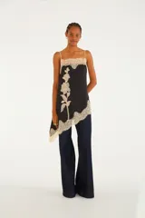 Blusa de breteles finos de color negro, con silueta amplia y caída asimétrica, confeccionada en tejido liviano con delicados detalles de encaje floral en el escote y el ruedo, y un gran aplique de encaje con diseño floral vertical en el frente.