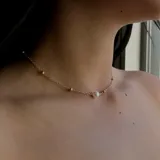 Gargantilla dorada con cadena fina y pequeñas cuentas doradas, con una perla central.