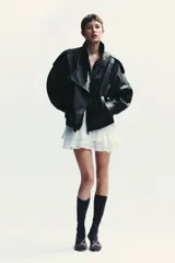 Vestido corto blanco de escote en V y manga larga con puños abotonados. Presenta volantes con bordados de encaje en el cuello, escote y falda. Cierre lateral con cremallera oculta.