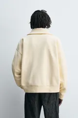 Sudadera color crema de algodón con interior afelpado, corte relajado, cuello subido y manga larga. Presenta bolsillos de vivo en la cadera y acabados en rib, con cierre frontal de cremallera.